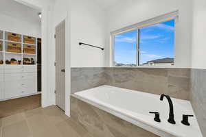 Primary Full bath with light tile patterned floors, a garden tub, a walk in closet, and light carpet