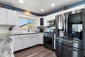 Kitchen with stainless steel appliances, white cabinets, dark wood-type flooring, and recessed lighting