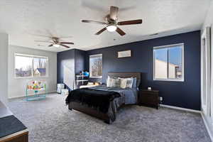 Carpeted bedroom with a textured ceiling, multiple windows, and a ceiling fan