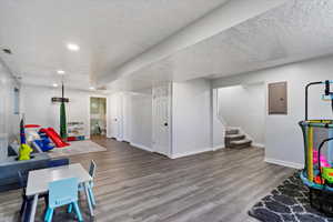 Rec room with wood finished floors, electric panel, a textured ceiling, and recessed lighting