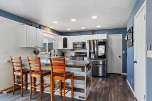 Kitchen featuring appliances with stainless steel finishes, white cabinetry, recessed lighting, a breakfast bar area, and dark wood-type flooring