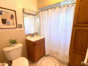 Full bathroom featuring vanity, tile walls, shower / bathtub combination with curtain, and a wainscoted wall