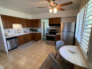Kitchen featuring appliances with stainless steel finishes, light floors, light countertops, ceiling fan, and exhaust hood