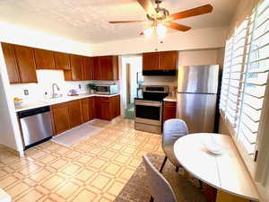 Kitchen featuring light flooring, appliances with stainless steel finishes, light countertops, a ceiling fan, and exhaust hood