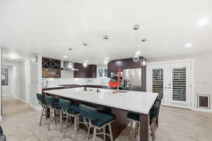 Kitchen with dark brown cabinetry, a spacious island, stainless steel refrigerator with ice dispenser, a breakfast bar, and hanging light fixtures