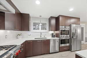 Kitchen with stainless steel appliances, backsplash, exhaust hood, decorative light fixtures, and dark brown cabinetry