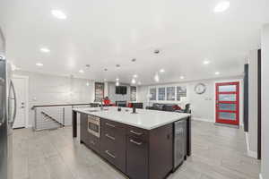 Kitchen featuring dark brown cabinetry, stainless steel appliances, open floor plan, decorative light fixtures, and recessed lighting