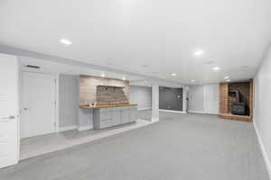 Unfurnished living room featuring a wood stove, light carpet, recessed lighting, and wet bar