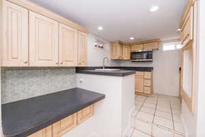 Kitchen featuring dark countertops, tasteful backsplash, stainless steel microwave, light brown cabinetry, and recessed lighting