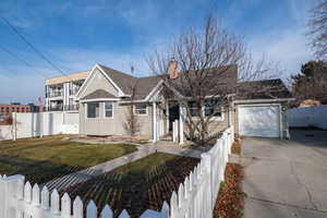 View of front of property featuring a fenced front yard, driveway, a shingled roof, a chimney, and a garage