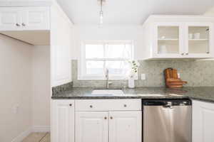 Kitchen with white cabinetry, dishwasher, dark stone countertops, and backsplash