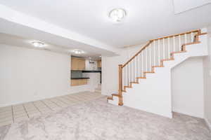 Unfurnished living room with light tile patterned floors, stairs, and light carpet