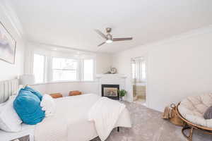 Bedroom featuring ornamental molding, a ceiling fan, a glass covered fireplace, carpet floors, and ensuite bathroom