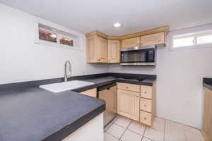 Kitchen featuring stainless steel appliances, dark countertops, light brown cabinets, and light tile patterned flooring