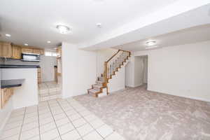 Unfurnished living room with light carpet, light tile patterned flooring, stairs, and recessed lighting