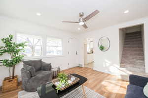 Living area with crown molding, light wood-style flooring, ceiling fan, recessed lighting, and stairway
