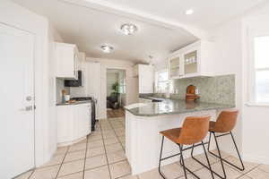 Kitchen with a peninsula, a breakfast bar, dark stone counters, backsplash, and recessed lighting