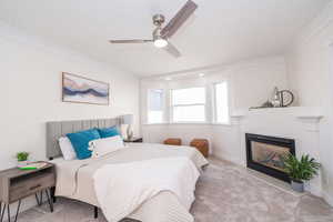 Bedroom featuring carpet flooring, a fireplace with flush hearth, ornamental molding, and a ceiling fan