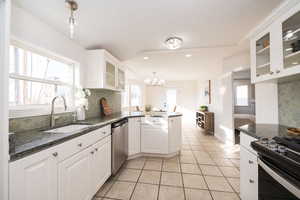 Kitchen featuring glass insert cabinets, decorative backsplash, a peninsula, white cabinetry, and dark stone countertops