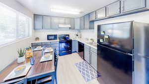 Kitchen featuring black appliances, light countertops, light wood-style flooring, under cabinet range hood, and gray cabinets