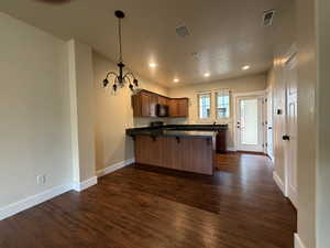 Kitchen featuring a peninsula, hanging lights, dark wood-type flooring, wood finish cabinetry, and dark stone counters
