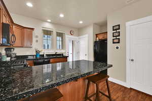 Kitchen with a peninsula, brown cabinets, a kitchen breakfast bar, black appliances, and dark wood-style floors