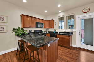Kitchen with brown cabinets, black appliances, a kitchen breakfast bar, a peninsula, and dark wood-style flooring