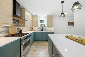 Kitchen with stainless steel stove, wall chimney range hood, pendant lighting, modern cabinets, and green cabinets