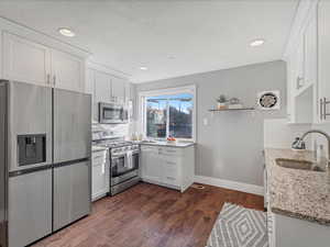 Kitchen with appliances with stainless steel finishes, white cabinetry, light stone counters, open shelves, and tasteful backsplash