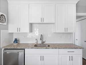 Kitchen featuring white cabinetry, stainless steel dishwasher, and light stone countertops