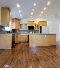 Kitchen featuring glass insert cabinets, vaulted ceiling, backsplash, stainless steel appliances, and a kitchen island