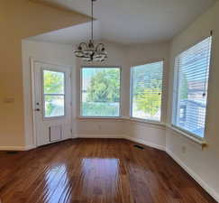 Unfurnished dining area featuring dark wood-style flooring, a chandelier, and vaulted ceiling