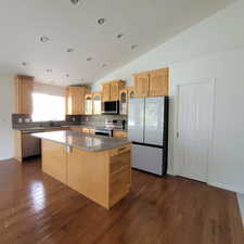 Kitchen with lofted ceiling, stainless steel appliances, glass insert cabinets, a center island, and dark stone countertops