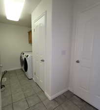 Laundry area with separate washer and dryer, light tile patterned floors, and cabinet space