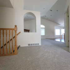 Carpeted spare room featuring vaulted ceiling and a chandelier