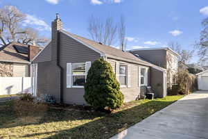 View of home's exterior featuring a chimney, concrete driveway, a detached garage, and an outbuilding