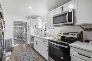 Kitchen with stainless steel appliances, white cabinets, light stone countertops, recessed lighting, and dark wood-style flooring