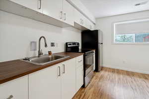 Kitchen featuring stainless steel electric range oven, white cabinetry, and light wood-style floors