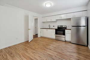 Kitchen with appliances with stainless steel finishes, white cabinetry, light wood-style flooring, and dark countertops