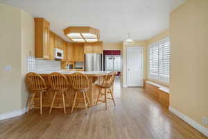 Kitchen with a breakfast bar, light countertops, a peninsula, backsplash, and light wood-style floors