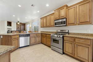Kitchen featuring appliances with stainless steel finishes, light stone counters, brown cabinetry, a peninsula, and recessed lighting