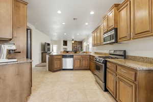 Kitchen featuring stainless steel appliances, light stone counters, open floor plan, a peninsula, and brown cabinetry