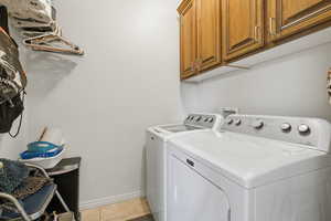 Laundry area featuring cabinet space, light tile patterned flooring, and separate washer and dryer