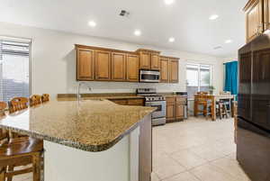 Kitchen featuring a kitchen breakfast bar, a peninsula, appliances with stainless steel finishes, brown cabinets, and light tile patterned floors