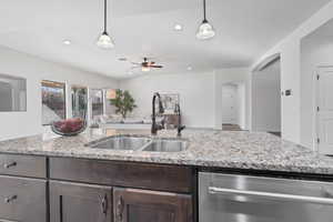 Kitchen with hanging light fixtures, dishwasher, dark brown cabinets, open floor plan, and light stone counters