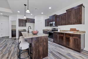 Kitchen with appliances with stainless steel finishes, light stone counters, hanging light fixtures, dark brown cabinets, and recessed lighting