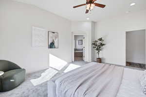 Carpeted bedroom with ensuite bathroom, ceiling fan, arched walkways, and lofted ceiling