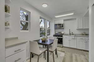 Kitchen featuring white cabinets, open shelves, light countertops, stainless steel appliances, and light wood-style flooring