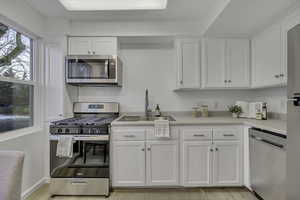 Kitchen featuring stainless steel appliances, white cabinetry, light countertops, and light wood-style flooring