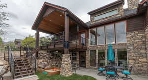 Rear view of house with stone siding, a patio, a wooden deck, and stairs